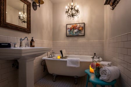 Soak in timeless charm—our primary suite’s ensuite features a vintage clawfoot tub, hand shower, and a dimmable chandelier for the perfect mood. Set with a book tray, it's your invitation to unwind in style.