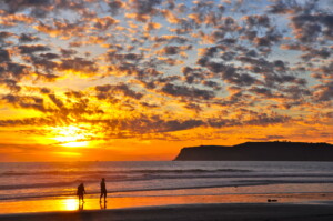 Golden sunset over a hidden cove in Orange County California, with waves gently washing over the sand and cliffs glowing in warm light.