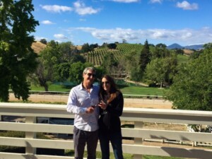 A couple enjoying a wine tasting outdoors at a boutique Los Olivos winery, surrounded by oak trees and vineyard views.