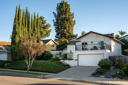 A charming hillside home with lush mature landscaping, private balcony patio, and clean modern exterior creating strong curb appeal and a welcoming residential feel.