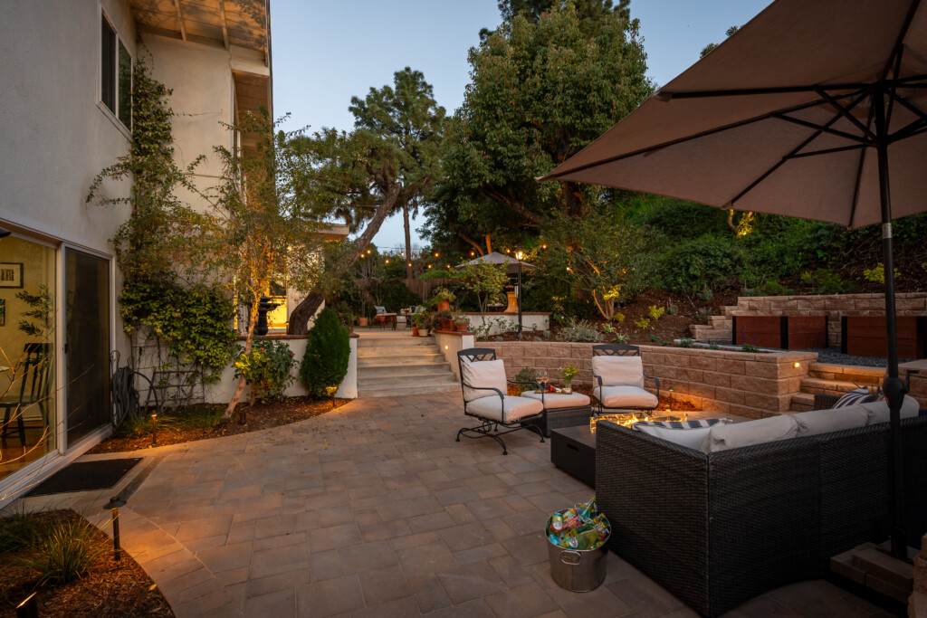 Inviting backyard retreat with layered patio seating, ambient lighting, and a warm fire feature. Ideal for evening gatherings and relaxed outdoor living.