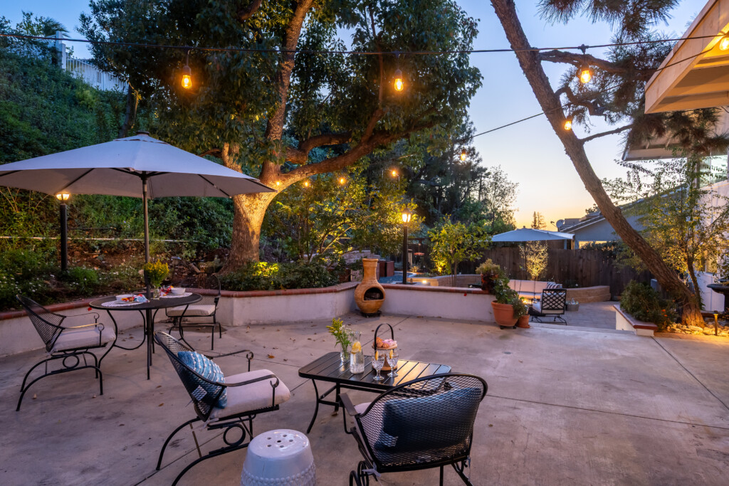 An inviting outdoor patio with café-style seating, glowing string lights, and layered garden terraces, creating a warm and intimate space for evening gatherings.