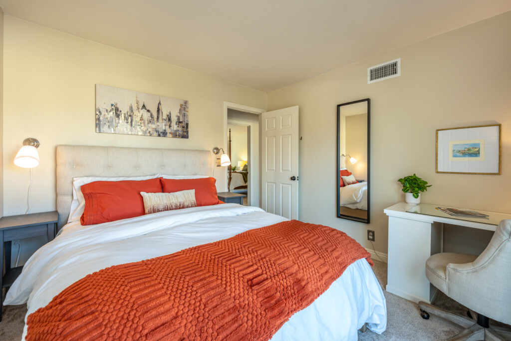 Inviting bedroom with soft linens, warm accent tones, and a dedicated desk for work or planning the day ahead. A comfortable space designed for both restful nights and productive mornings.